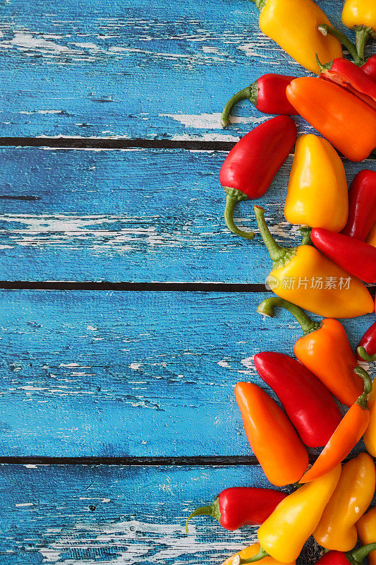 整个红、黄、橙迷你辣椒(Capsicum annuum)的海报边框设计特写图片，蓝色木纹背景，复制空间